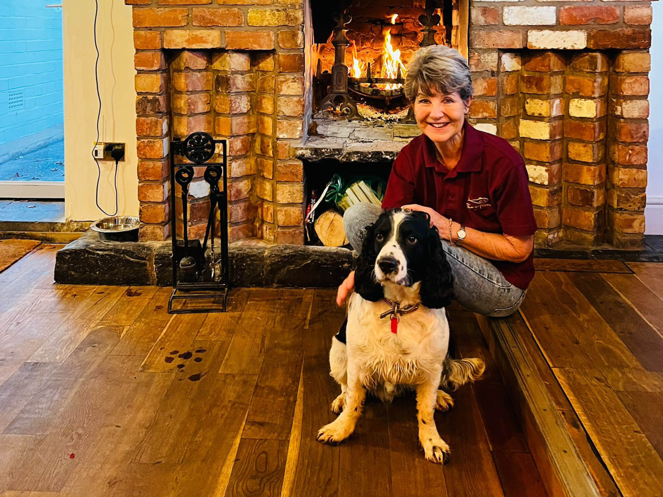 Owner of The Fish, Wixford sat infront of a fireplace with the pub dog.